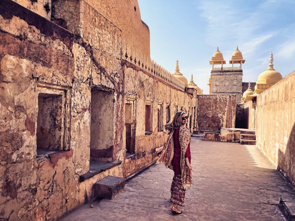 vista-trasera-de-una-mujer-madura-con-gafas-de-sol-y-ropa-tradicional-caminando-por-un-edificio-antiguo